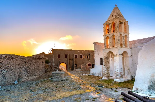 Alte Ruinen in einem verlassenen Dorf auf Kythira, während im Hintergrund langsam die Sonne versinkt.