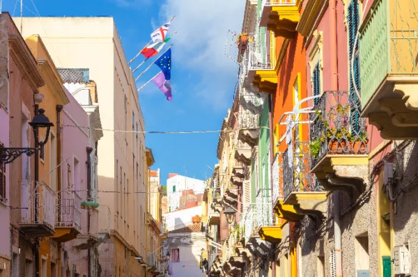 Eine rustikale Gasse in Carloforte am Tag mit bunten Hausfassaden und verschiedenen, gehissten Flaggen.