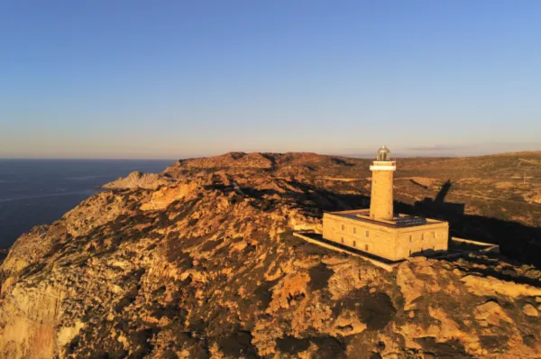 Der alte Leuchtturm von Carloforte auf San Pietro in der Abendsonne, umgeben von hügeligem Terrain.