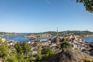 Blick auf die Dächer und den Kirchturm der norwegischen Stadt Arendal, im Hintergrund das Meer.