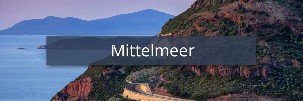 Ein Berg mit Serpentinen am Abend mit Aussicht auf das Meer und entfernte Berge.