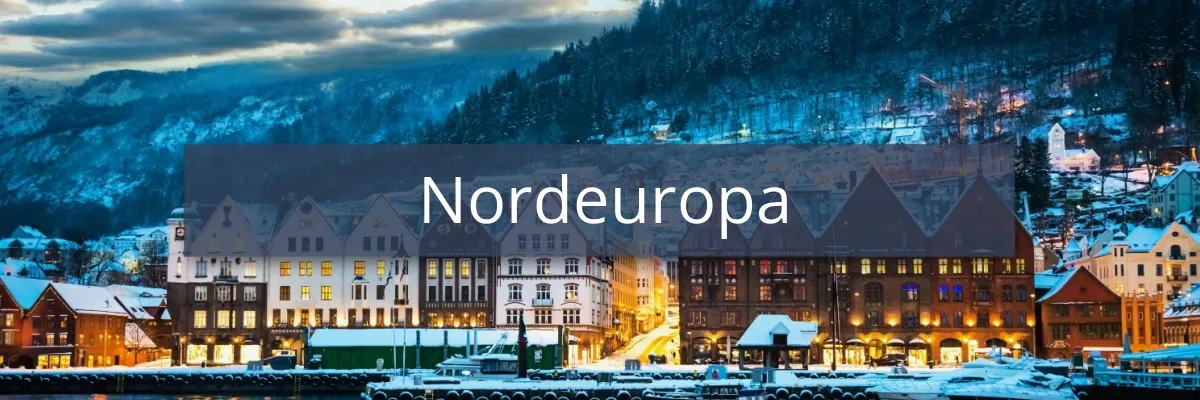 Norwegische Häuser bei Nacht an der Küste mit verschneiten Bergen im Hintergrund.