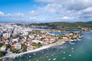 Blick auf die Küste von Cabo Frio am blauen Meer, im Hintergrund grüne hügelige Landschaften.