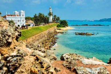 Küstenabschnitt in Galle mit Blick auf ein weißes Gebäude und einen Leuchtturm.