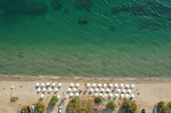 Vogelperspektive auf den Strand Drepano mit hellem Sand und weißen Sonnenschirmen.