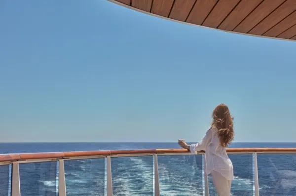 Eine Frau steht auf einem Außendeck von Explora Journeys und schaut auf das Meer.