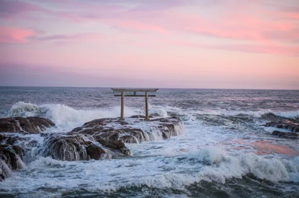 Ein Shinto-Schrein steht auf einem Felsen im Meer bei Sonnenuntergang.