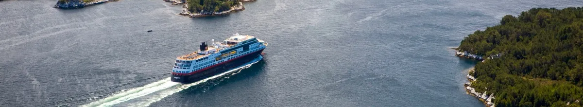 Die MS Midnatsol fährt an der Küste Norwegens entlang und hinterlässt Wellen im Meer.