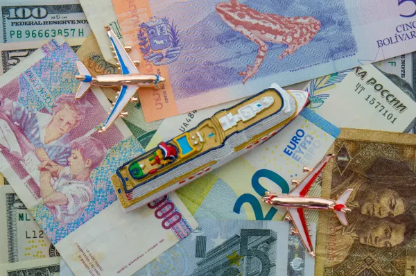 Spielzeug-Kreuzfahrtschiff und Flugzeuge auf verschiedenen internationalen Geldscheinen als Symbol für Reisebudgets und Tarife.