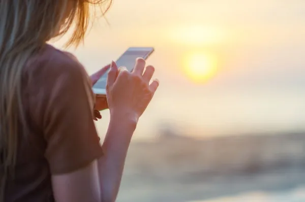 Eine Frau reist mit AIDA und kann dank der Internet-Flat weiterhin Ihre Social Media Kanäle pflegen. Der Sonnenuntergang im Hintergrund ist das perfekte Motiv.