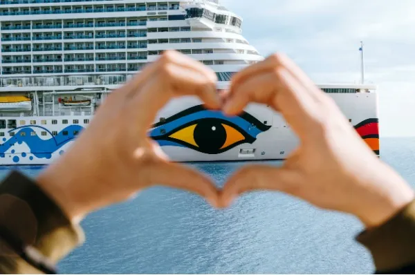 Eine Person formt ein Herz mit den Händen und umschließt dabei das AIDA Auge auf dem Schiff.
