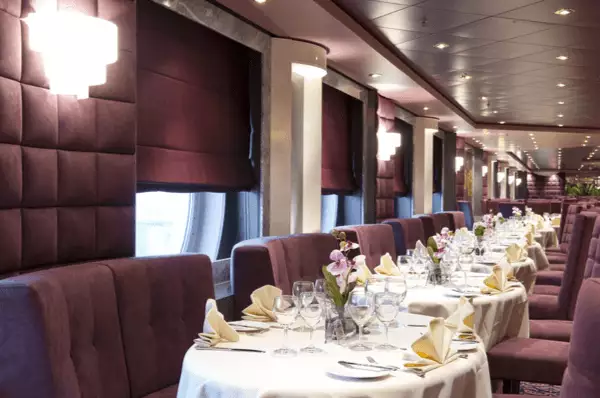 Ein Restaurant auf der MSC Magnifica mit aufwändig gedeckten, runden Tischen und Polstermöbeln.
