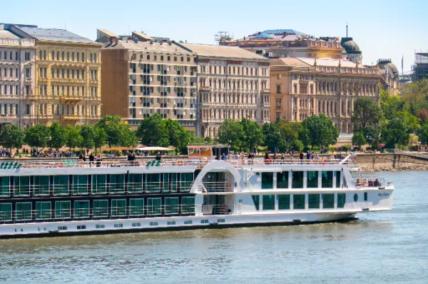 Passagiere auf dem Sonnendeck am Bug der MS VistaNova während der Fahrt auf der Donau vor der historischen Uferpromenade von Budapest.