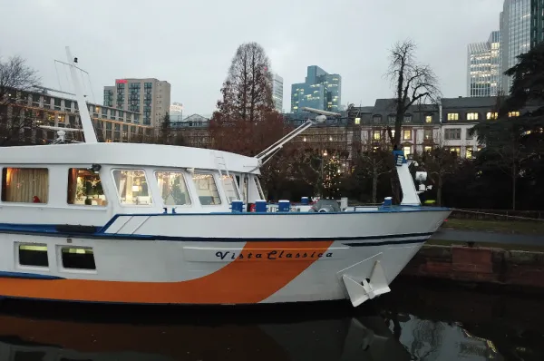 Bug der MS VistaClassica in einem Stadthafen Nahaufnahme vom Bug des Flusskreuzfahrtschiffes MS VistaClassica, das an einem Kai liegt. Im Hintergrund ist eine Parkanlage und die Skyline einer Stadt zu sehen.