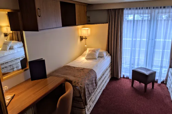 Einzelkabine auf der MS VistaClassica Ansicht einer gemütlichen Einzelkabine auf der MS VistaClassica mit Bett, Schreibtisch und einem großen Fenster mit Vorhängen, das auf den französischen Balkon führt.