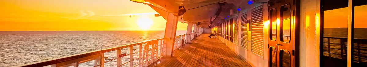 Sonnenuntergang auf dem Promenadendeck – Kreuzfahrt-Feeling pur Blick entlang eines beleuchteten Promenadendecks mit Holzplanken auf einem Kreuzfahrtschiff bei Sonnenuntergang über dem Meer.