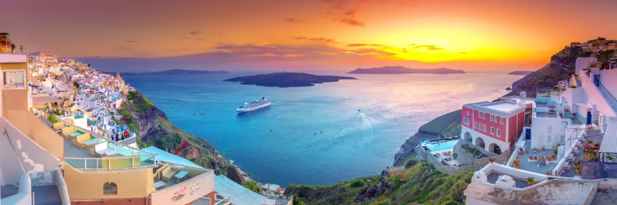 AIDA Mittelmeer Kreuzfahrt – Spektakulärer Sonnenuntergang auf den griechischen Inseln Weiß getünchte Häuser an den Klippen von Santorin bei Sonnenuntergang mit Blick auf ein Kreuzfahrtschiff im Meer.
