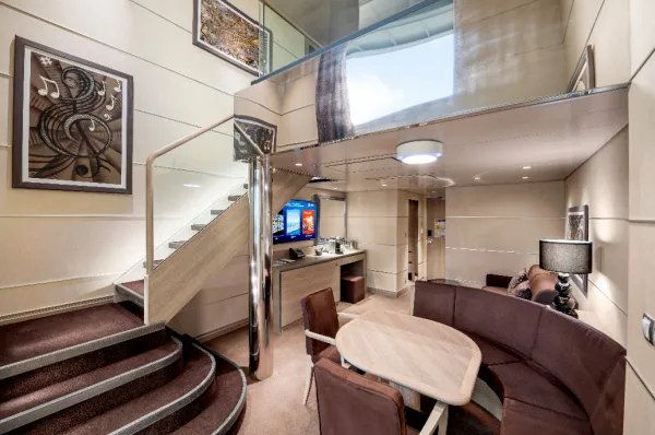 Innenansicht einer luxuriösen zweistöckigen Duplex Suite des MSC Yacht Clubs auf der MSC Virtuosa, mit einer eleganten Wendeltreppe zum oberen Schlafbereich und einem Wohnbereich mit Sofa und Esstisch im unteren Bereich.