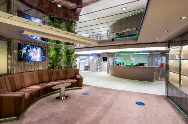 Der moderne Empfangs- und Wartebereich des MSC Aurea Spas an Bord der MSC Virtuosa, mit einer geschwungenen Rezeptionstheke, einer großen Couch und einer spiegelnden Decke.