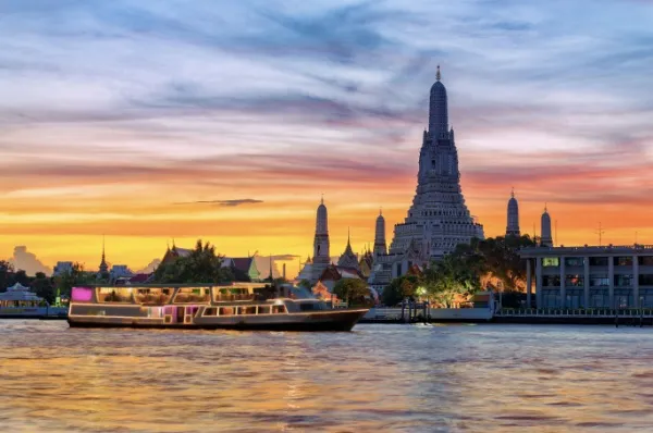 Ein Schiff gleitet am Ufer Bangkoks entlang, während im Hintergrund der Wat Arun Tempel zu sehen ist.
