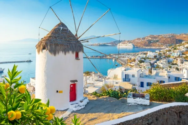Mykonos mit blau weißen Häusern am Meer, im Vordergrund eine alte kleine Windmühle.