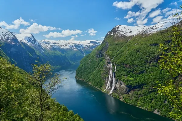 Der Geirangerfjord - blaues Wasser inmitten grüner Berglandschaften unter blauem Himmel.