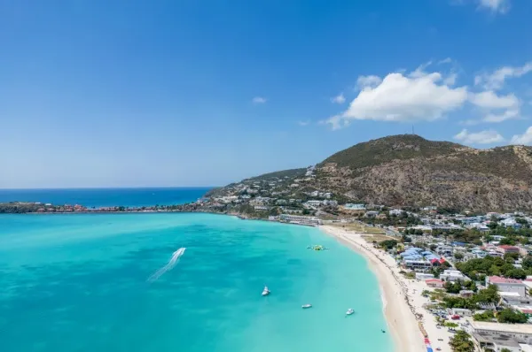 Türkisfarbenes Wasser und Sandstrand, im Hintergrund Gebirge.