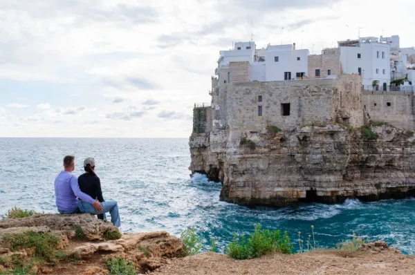 Ein Paar sitzt auf einem Felsvorsprung und blickt auf Meer und Altstadt.