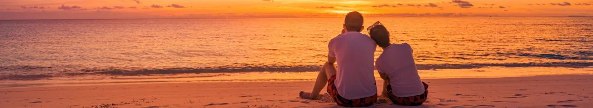 Ein Paar sitzt am Strand und blickt auf den Sonnenuntergang über dem Meer.