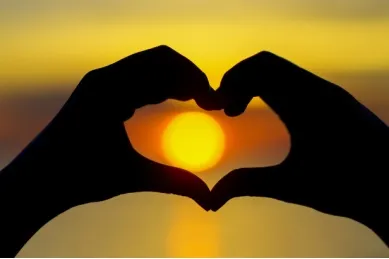 Silhouette von zwei Händen, die ein Herz vor Sonnenuntergang formen.