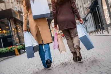 Zwei Frauen mit Einkaufstüten laufen durch eine Shopping-Straße.
