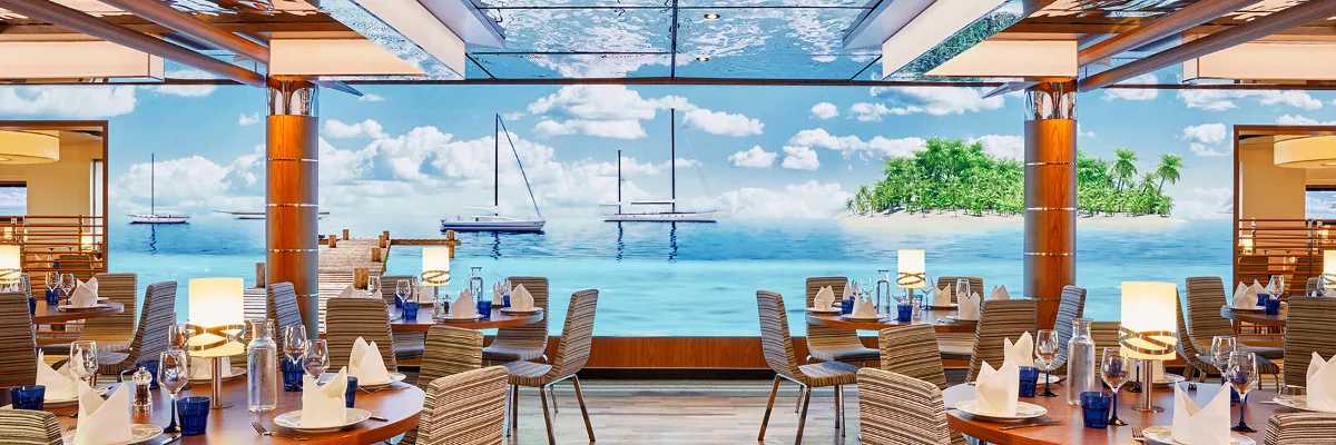 Kulinarische Vielfalt an Bord: Spezialitäten- und Buffetrestaurants über MyAIDA reservieren Elegantes Restaurant mit maritimem Panoramafenster an Bord von AIDAprima zur Tischreservierung im MyAIDA Reiseportal.