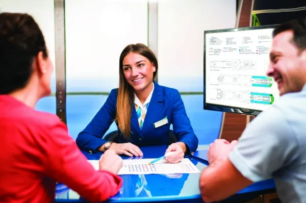 Costa C|Club Eine Costa-Mitarbeiterin sitzt gegenüber von einem Mann und einer Frau und erklärt ihnen etwas.