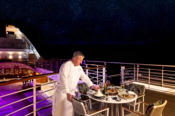 Ein Koch serviert Essen auf Deck unter dem Nachthimmel.