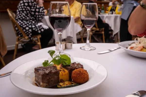 Feines Essen und zwei Rotweingläser auf einem gedeckten Tisch mit weißer Tischdecke.