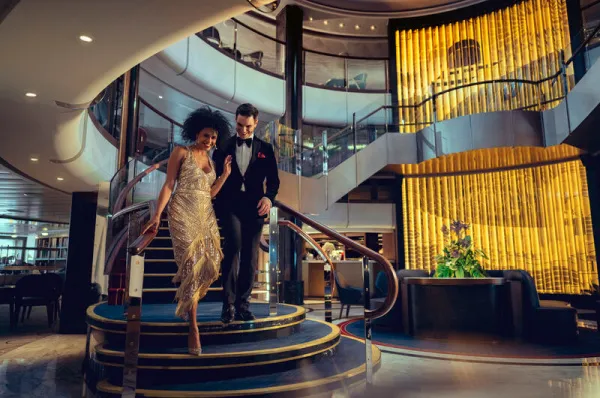 Ein elegant gekleidetes Paar in Abendgarderobe steigt die große Treppe im Atrium eines luxuriösen Cunard-Schiffes hinab.
