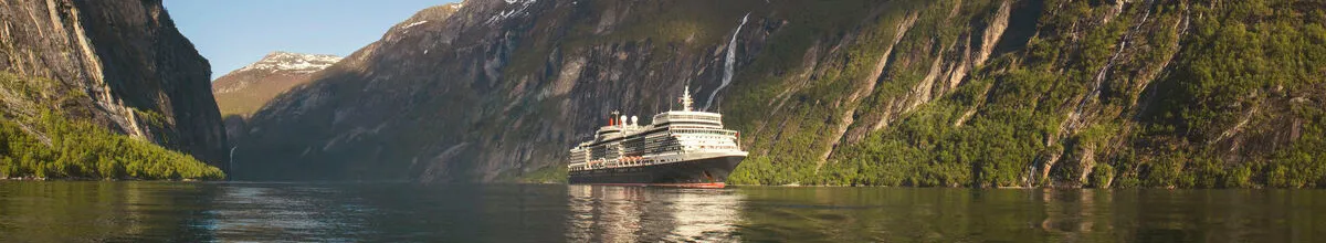 Eine Panoramaaufnahme eines Cunard-Kreuzfahrtschiffs, das durch einen engen, majestätischen Fjord fährt. Steile, begrünte Berge ragen auf beiden Seiten empor, von denen dünne Wasserfälle herabstürzen, während sich das Schiff im ruhigen Wasser spiegelt.