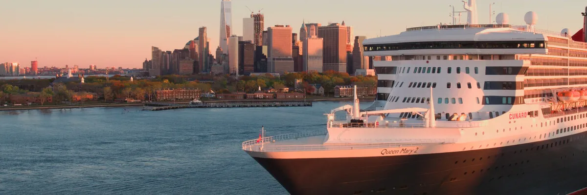 Eine Panoramaaufnahme des Cunard-Kreuzfahrtschiffs Queen Mary 2, das im Hafen von New York vor der Skyline von Lower Manhattan liegt.