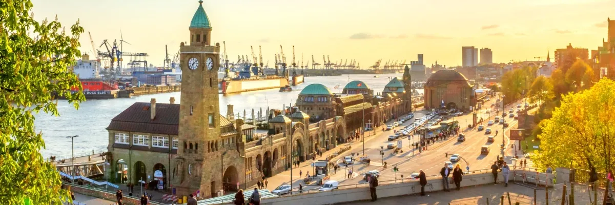Blick auf die St. Pauli Landungsbrücken im Hamburger Hafen. Im Vordergrund ist der Pegelturm mit Uhr zu sehen. Im Hintergrund befinden sich zahllose Kräne.