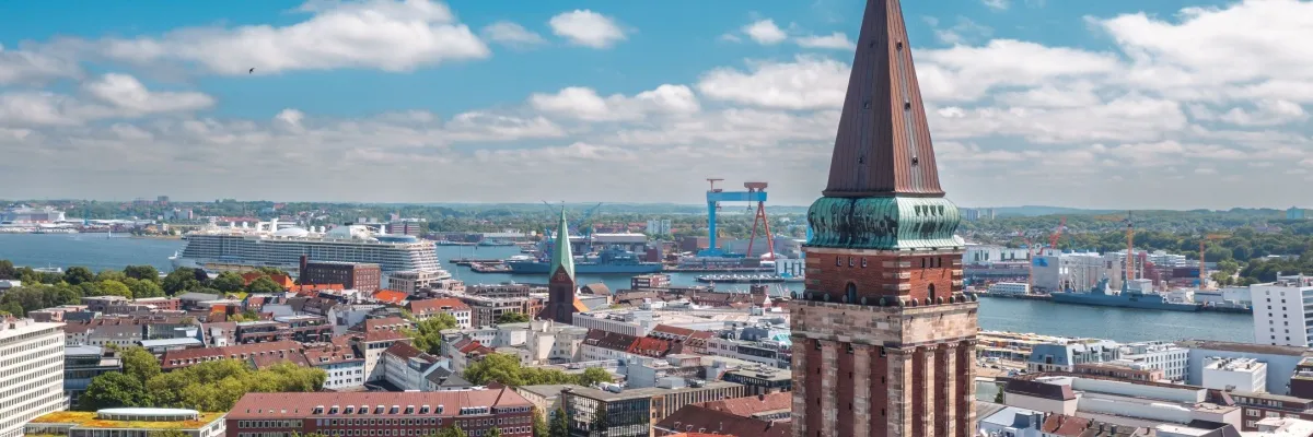 Kreuzfahrtschiffe im Hafen von Kiel. Im Vordergrund der Rathausturm, dahinter Häuser und ein Kirchturm.