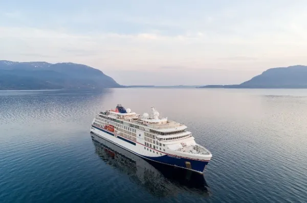 Ein Schiffsmotiv vom Schiff HANSEATIC nature im blauen Wasser mit Bergen im Hintergrund.