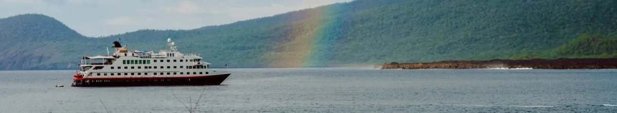 Die MS Santa Cruz II auf dem Wasser, ein leichter Regenbogen schimmert über das Wasser im Hintergrund Berge.