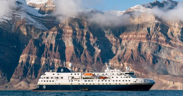 Die MS Spitsbergen vor steinigen Berglandschaften auf dem Wasser.