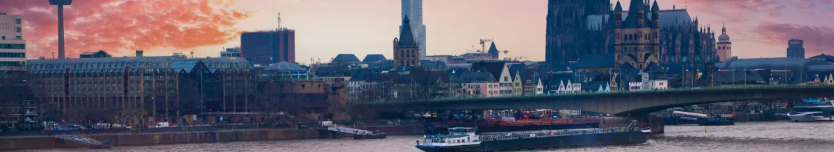 Panoramablick auf die Kölner Skyline mit Dom, Groß St. Martin und der Deutzer Brücke bei Sonnenuntergang am Rhein.