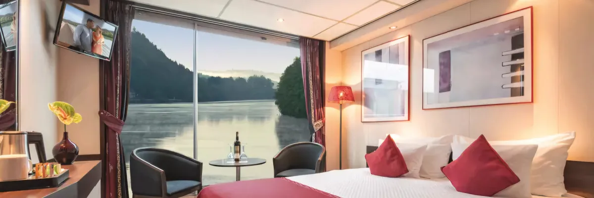 Blick in eine komfortable 1A Vista Außenkabine mit Doppelbett, Sitzecke und großem Panoramafenster mit Aussicht auf den Rhein.