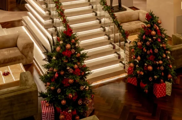 Zwei nachhaltig dekorierte Weihnachtsbäumen mit Geschenken schmücken eine beleuchtete Treppe auf einem der Explora Schiffe.