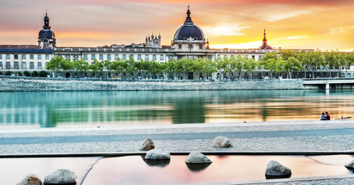 Blick auf das Ufer der Rhône, im Hintergrund Gebäude der Stadt Lyon bei Sonnenuntergang.