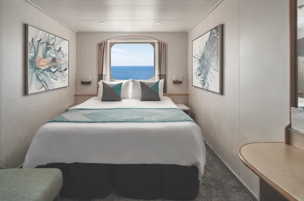 Außenkabine Norwegian Cruise Line Außenkabine mit kleinem Fenster an Bord der Norwegian Sky mit einem Queen-Size-Bett unter dem Fenster.