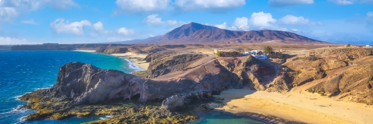 Zauberhafte Kanaren-Kreuzfahrten zum Travel Tuesday Küste der Kanareninsel Lanzarote mit Stränden, vulkanischer Landschaft und dem tiefblauen Atlantik am linken Bildrand.