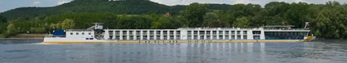 Das renovierte schiff Ms VistaDiamond schippert auf der Donau, von der Seite fotografiert, und passiert ein Waldstück am Ufer.